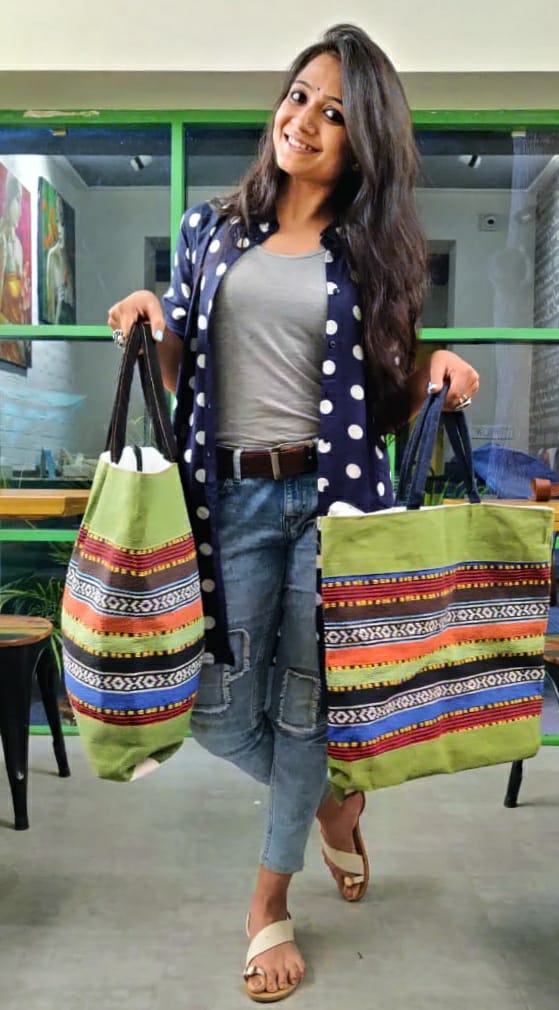 Customer holding two green jute tote bags with colourful woven stripes