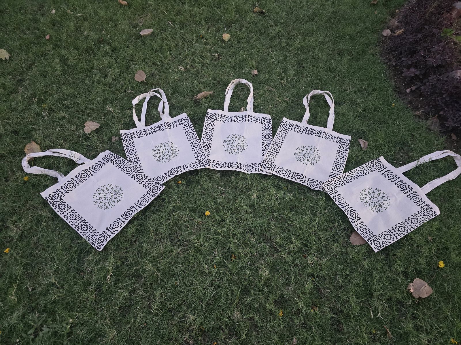 Five block-printed cotton tote bags laid out on grass